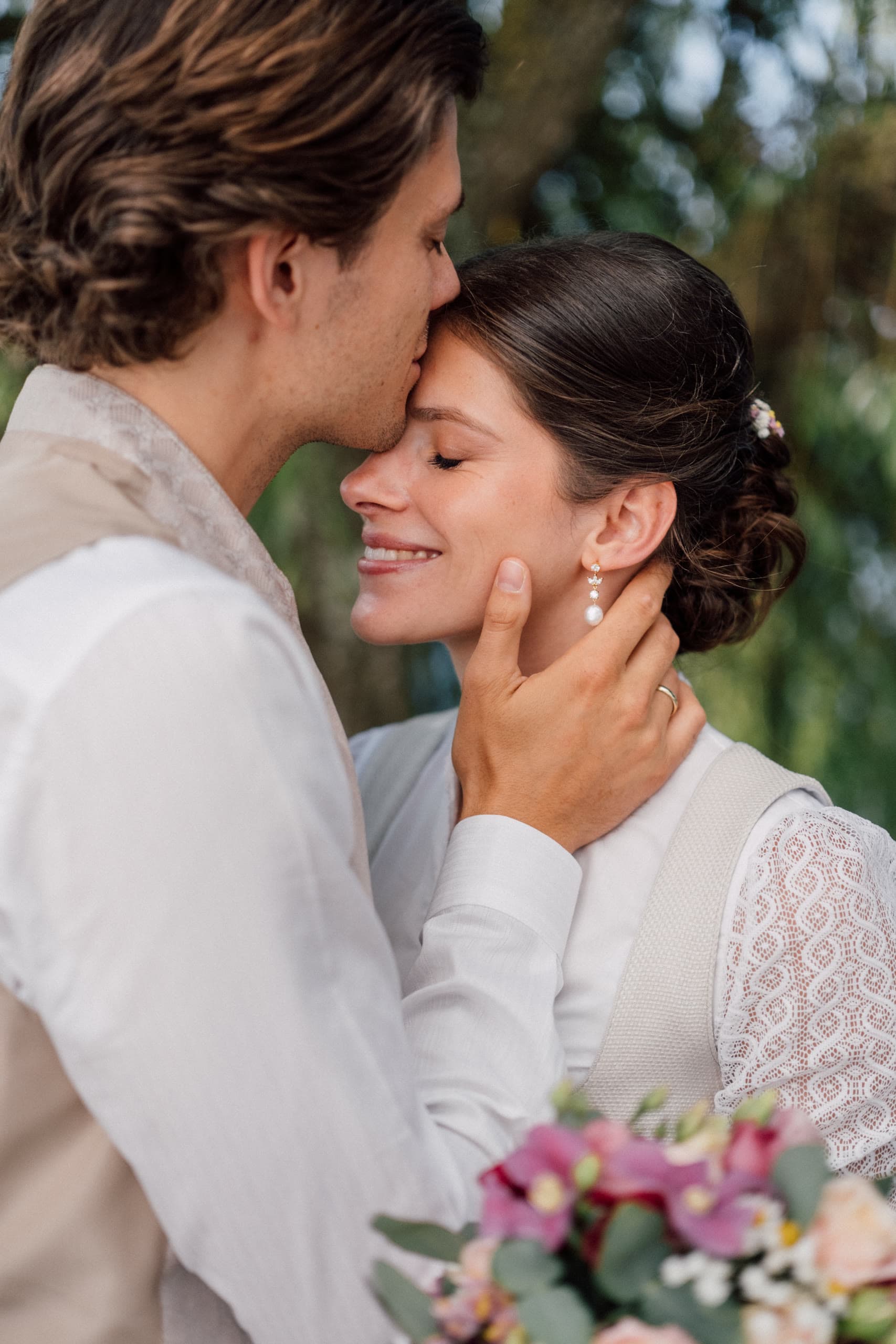 Groom kisses the bride's forehead while cupping her face, both smiling